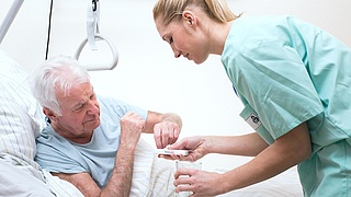 Krankenschwester reicht einem Mann im Krankenhausbett Tabletten.