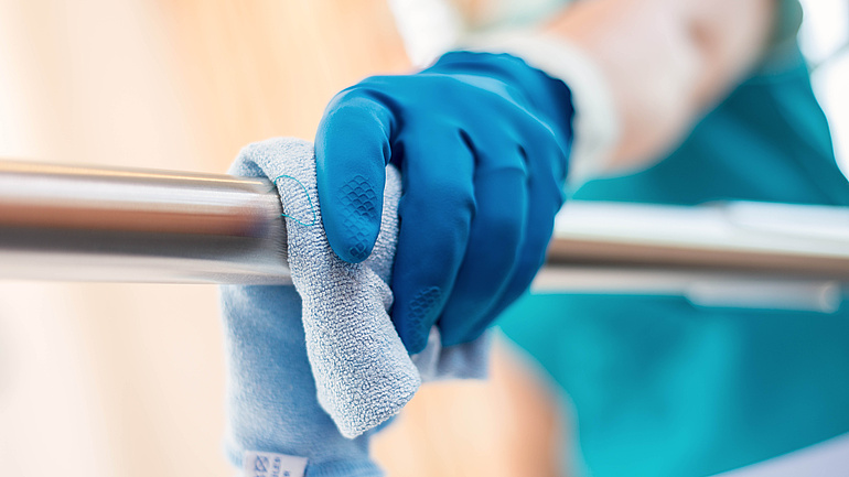 Eine Hand reinigt den Griff eines Krankenbettes mit einem Lappen.