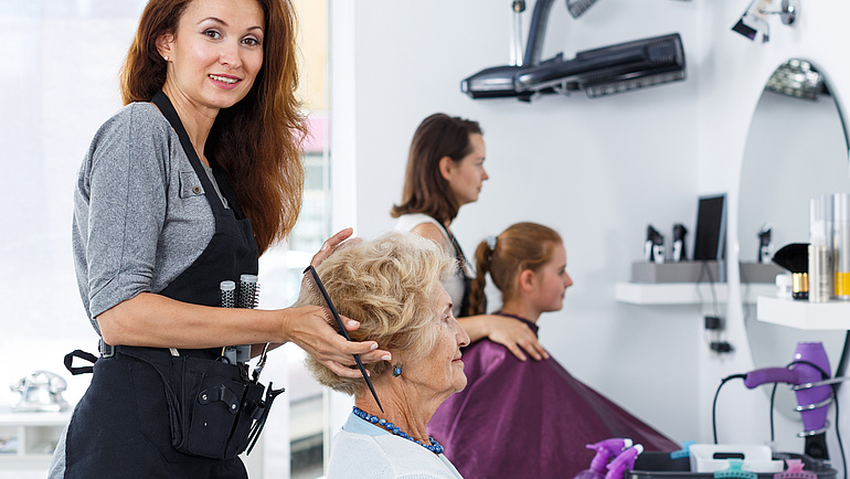 Eine Friseurin im Salon frisiert einer Seniorin die Haare.