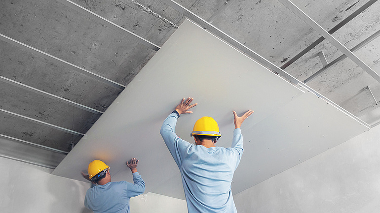 Bauarbeiter bringen Dachplatten innen an einer Decke an.