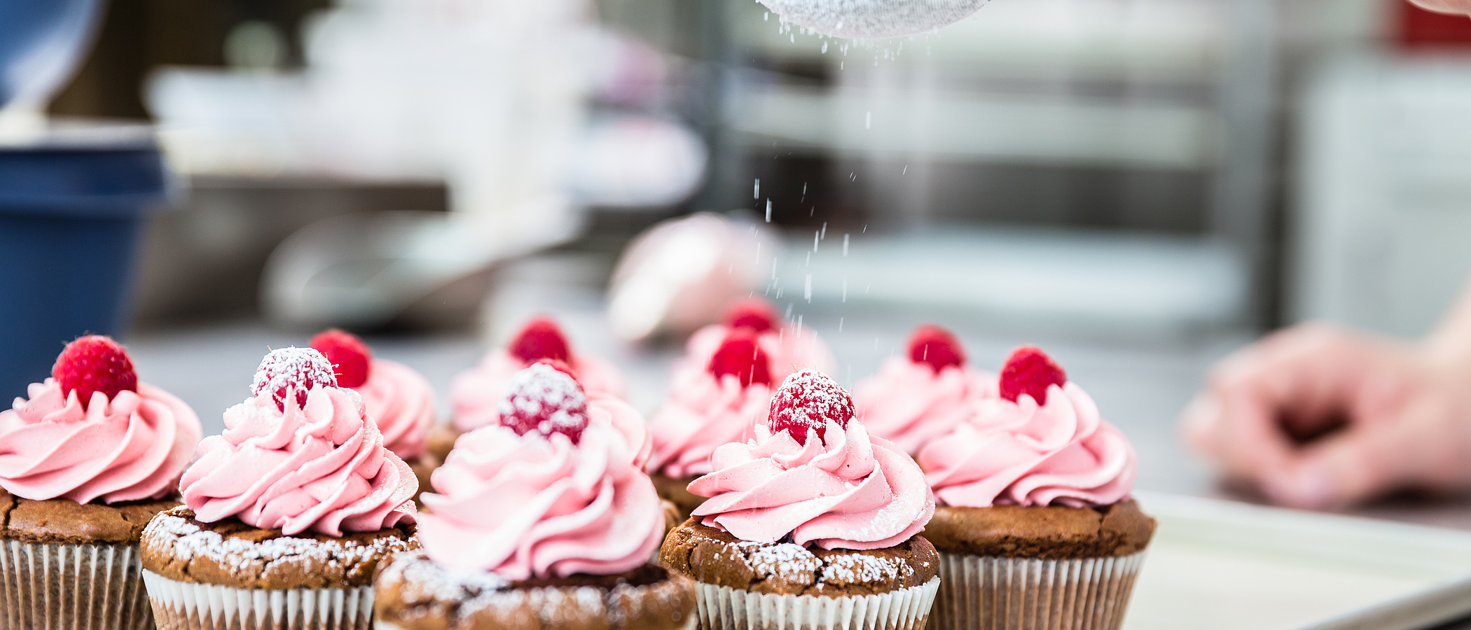 Himbeermuffins auf einem weißen Teller werden mit Puderzucker bestäubt.