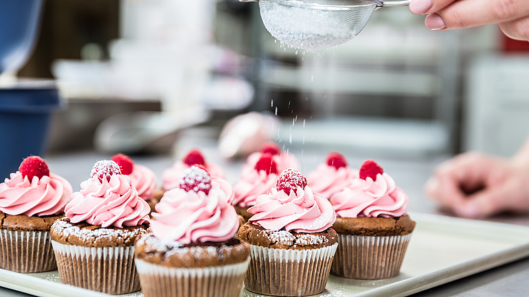 Himbeermuffins auf einem weißen Teller werden mit Puderzucker bestäubt.